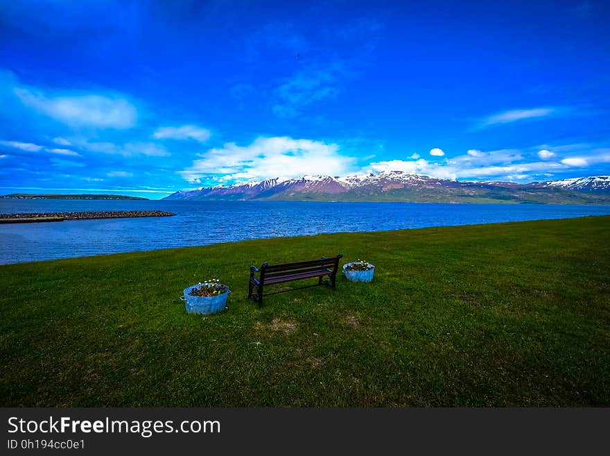 A bench by the shore with a mountain range in the distance. A bench by the shore with a mountain range in the distance.