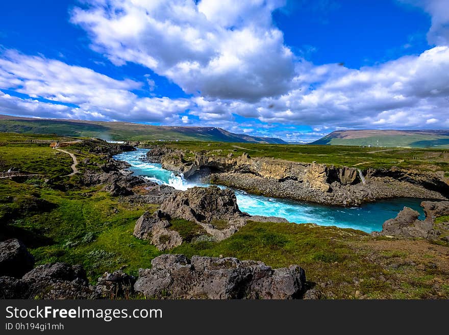 Aerial view of river with rocky banks through green field in countryside with blue skies and white clouds. Aerial view of river with rocky banks through green field in countryside with blue skies and white clouds.