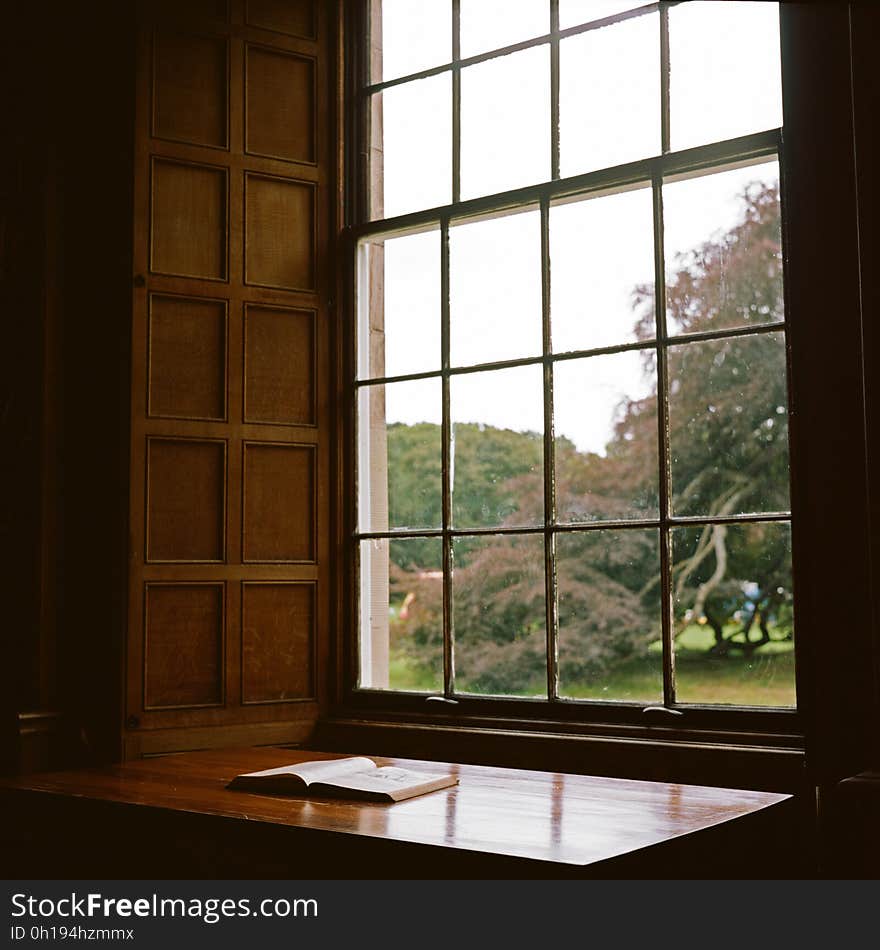 Open book on wooden table next to sunny window inside home. Open book on wooden table next to sunny window inside home.