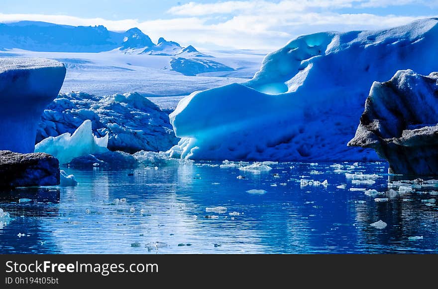 Icebergs floating in water along edge of glacier on sunny day. Icebergs floating in water along edge of glacier on sunny day.