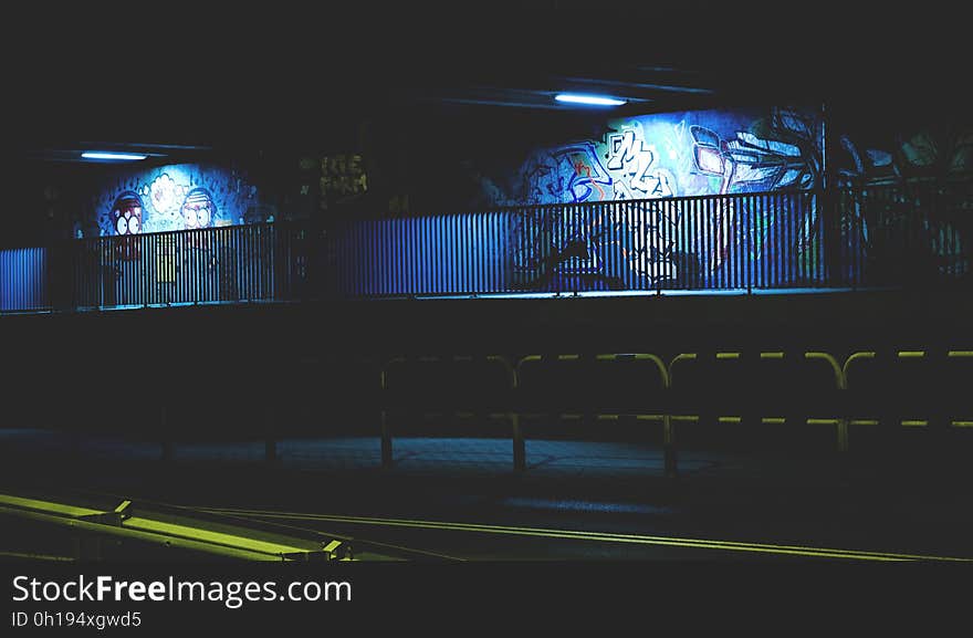 A view of a street at night with graffiti on the walls lit by the streetlights. A view of a street at night with graffiti on the walls lit by the streetlights.