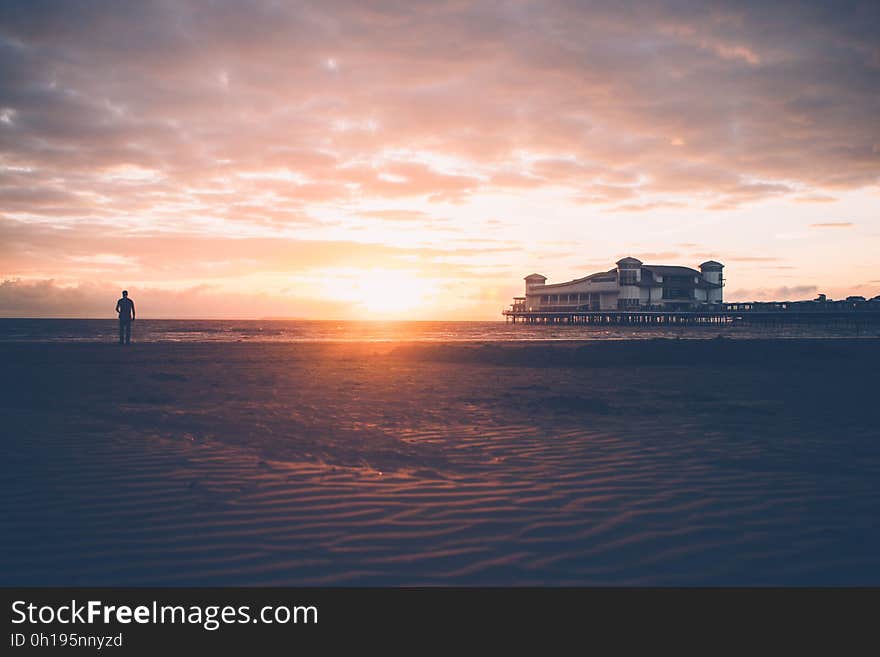 A sunset on a beach with a person looking at the sea. A sunset on a beach with a person looking at the sea.