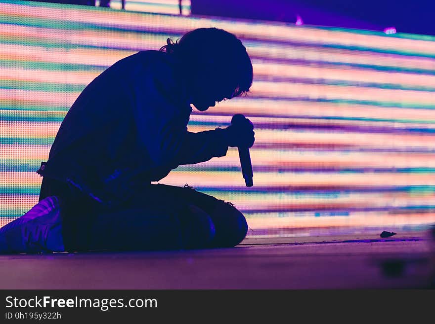 Side view of silhouetted person singing with microphone bright corrugated effect background.