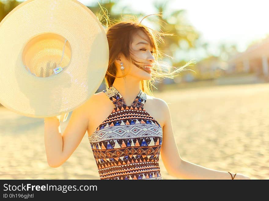 A portrait of a young smiling woman on a beach holding a hat. A portrait of a young smiling woman on a beach holding a hat.