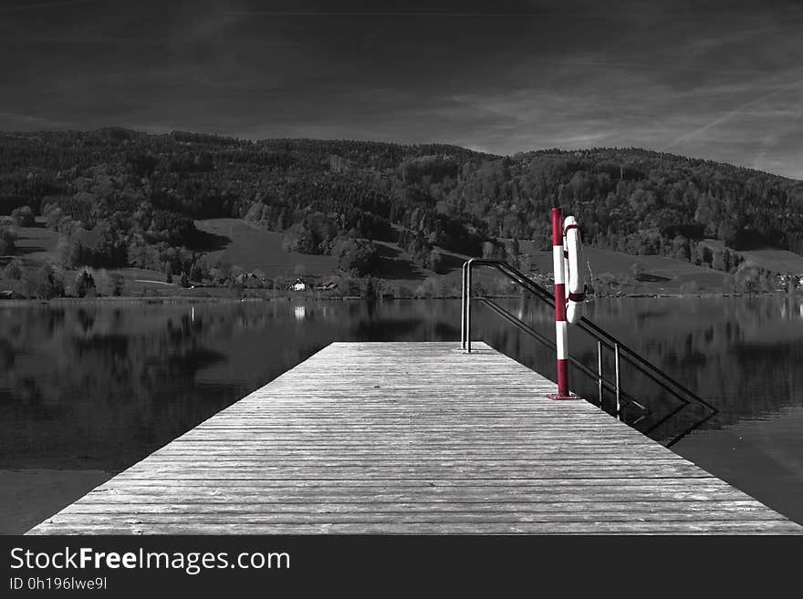 A selective color photo of a lake with a pier. A selective color photo of a lake with a pier.