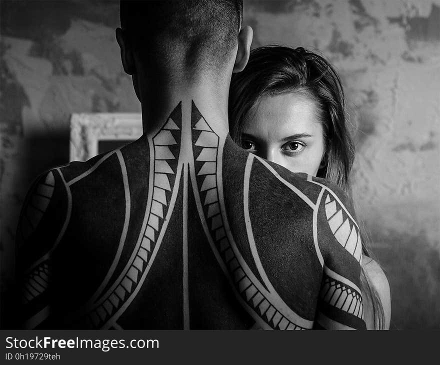 Black and white closeup of man with tattooed back, woman looking over shoulder. Black and white closeup of man with tattooed back, woman looking over shoulder.