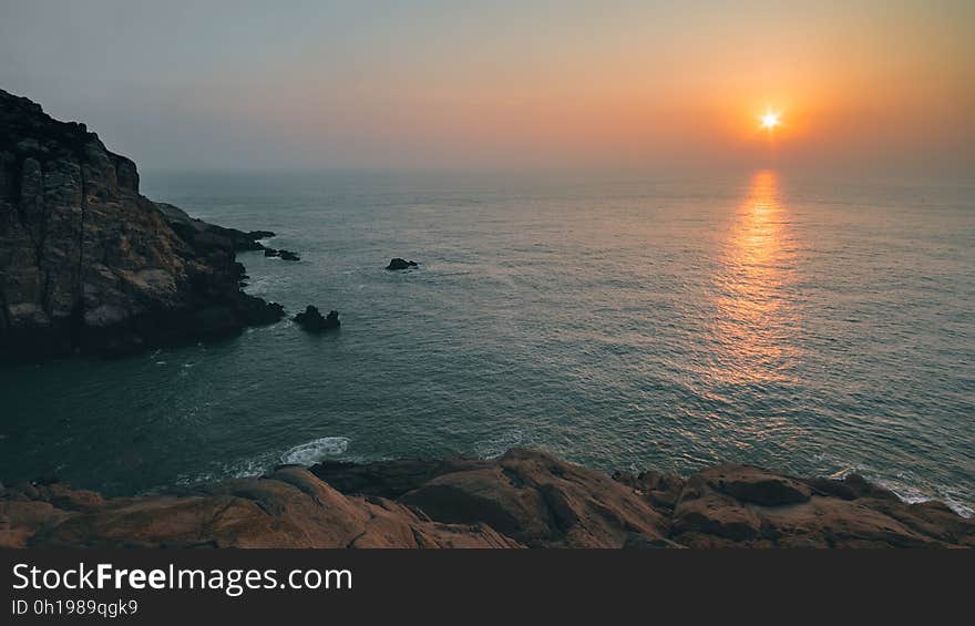 A view of a rocky coast with the sun rising in the distance. A view of a rocky coast with the sun rising in the distance.