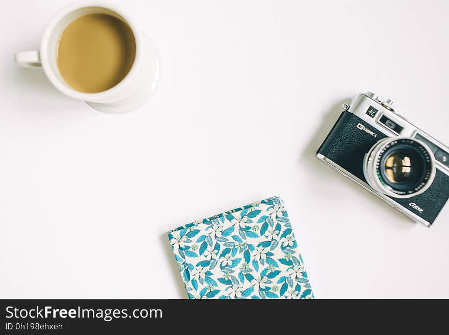 A tabletop with a cup of coffee, notepad and a classic style camera. A tabletop with a cup of coffee, notepad and a classic style camera.