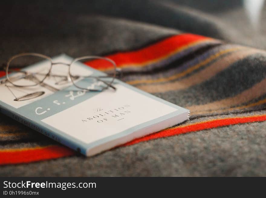 Spectacles resting on paperback book with blanket in background. Spectacles resting on paperback book with blanket in background.