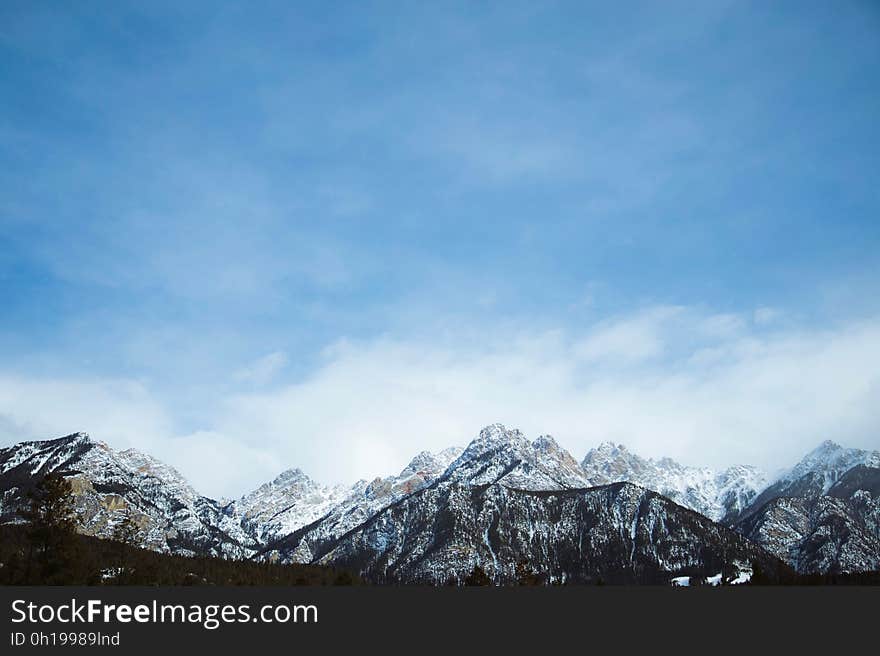 Scenic view of snow capped mountain range with blue sky and cloudscape background.