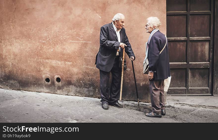 Elder man and woman with cane standing outside building having conversation on sunny day. Elder man and woman with cane standing outside building having conversation on sunny day.