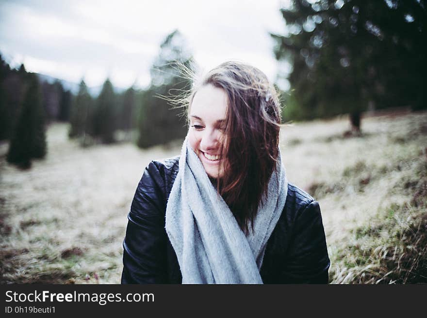 Portrait of smiling woman wearing fall jacket and scarf standing in field of sunny forest. Portrait of smiling woman wearing fall jacket and scarf standing in field of sunny forest.