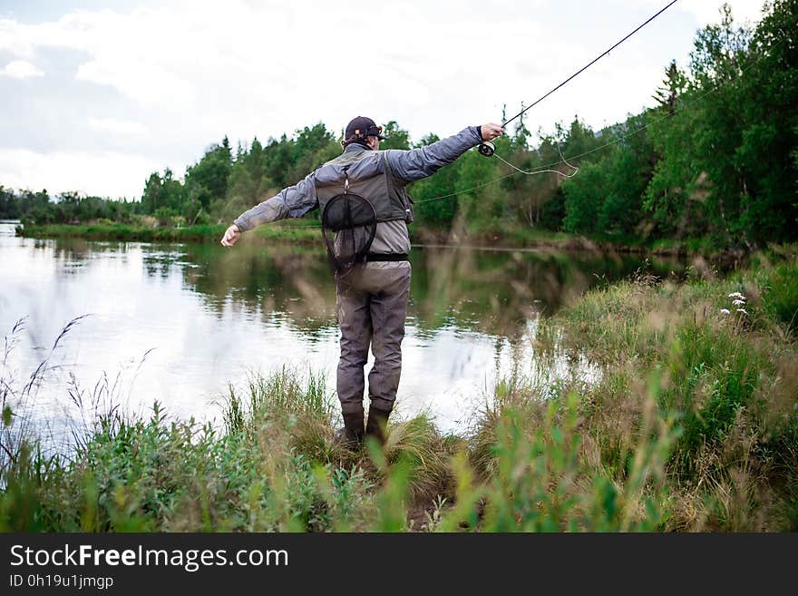 Man in Brown Pants Casting Fishing Rod Into Lake