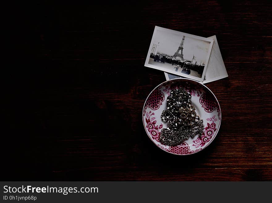 Silver Chain Accessory on White and Purple Ceramic Plate Near Grayscale Eiffel Tower Picture