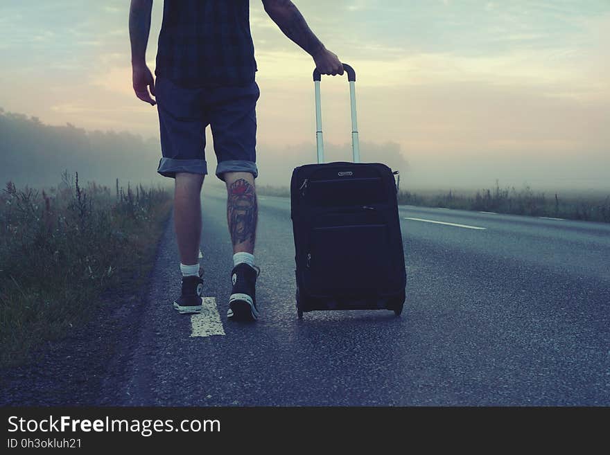 Man Walking on the Road Holding Black Luggage during Sunset