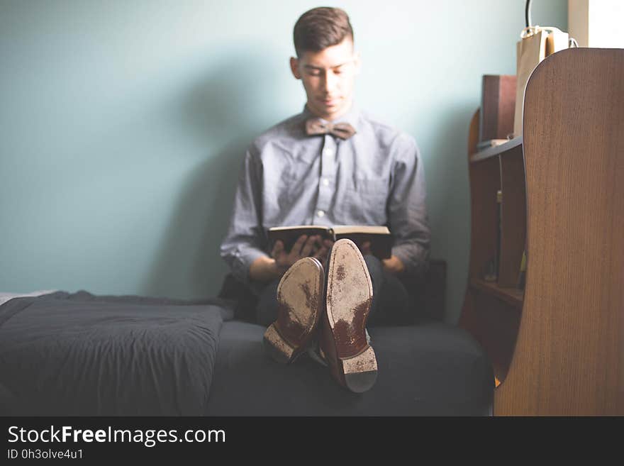 Man in Purple Dress Shirt Sitting on Bed Holding Books