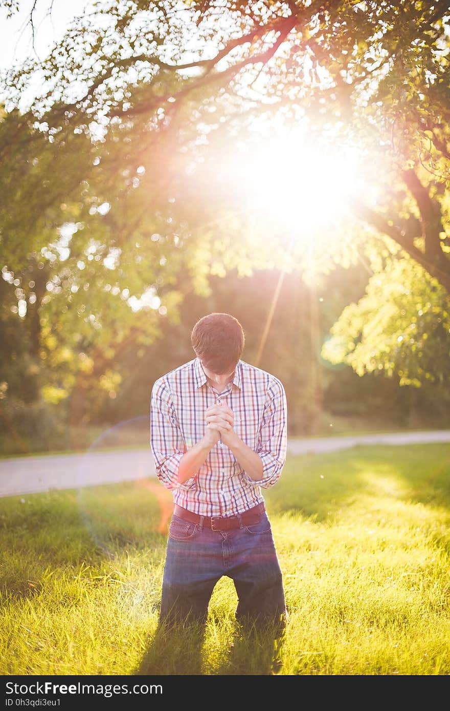 Man Wearing Longsleeves Shirt and Denim Jeans Kneeling on Grass during Daytime