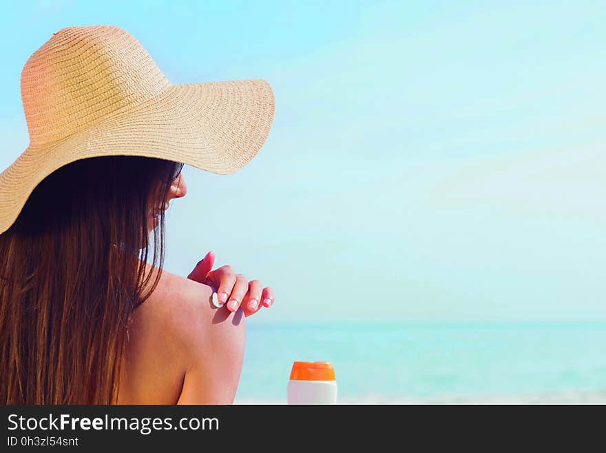 Brunette putting sunscreen on her shoulder on beach