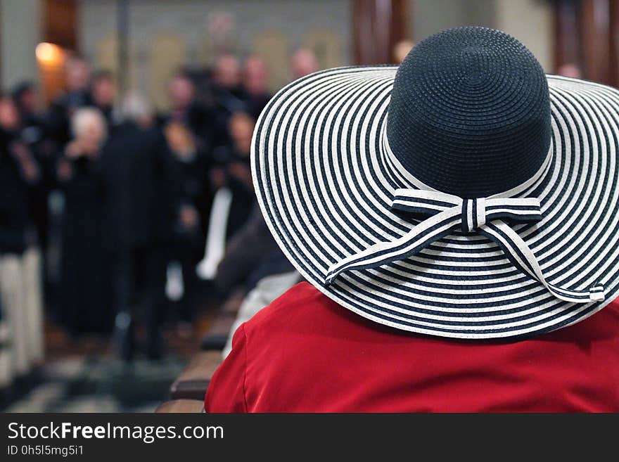 Woman in Red Shirt and Black and White Stripes Sunhat Surrounded by People