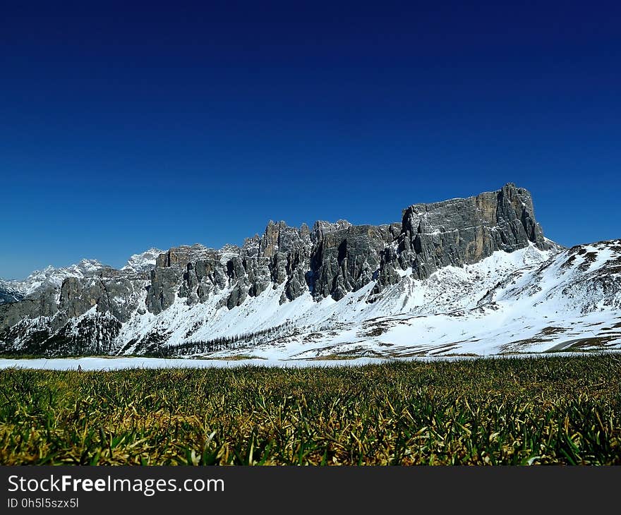 Green Fields Under Grey Rock Formations Covered With Snow