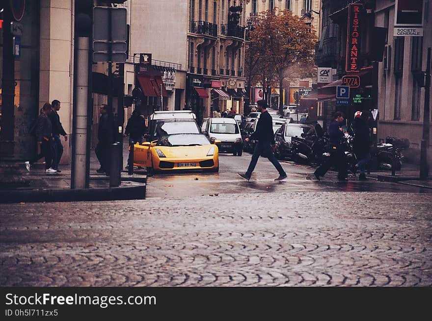 Person Walking Across the Street in Front of Yellow Sports Car during Daytime