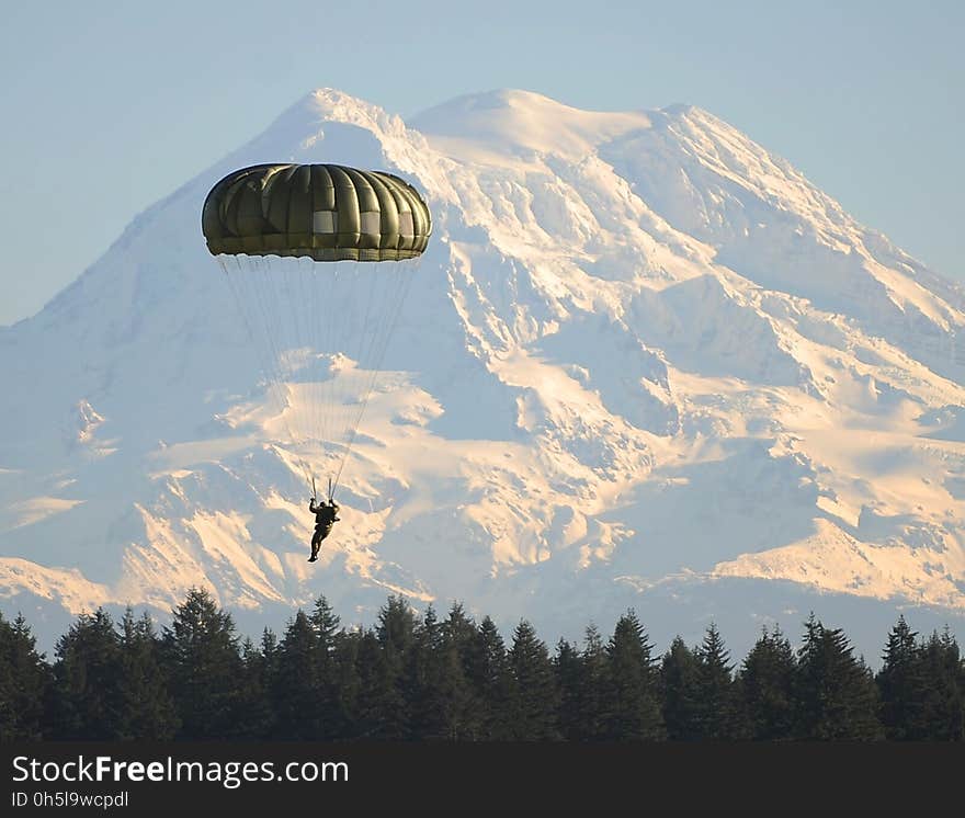 Man Flying on Parachute Near Green Trees