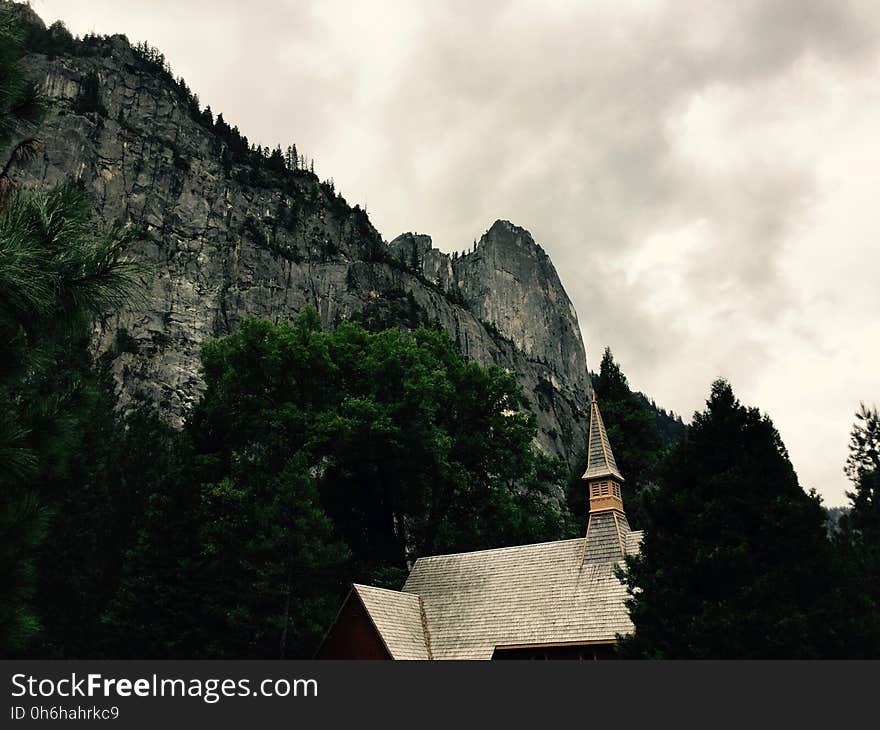 White House Near Grey Mountain and Green Trees during Daytime