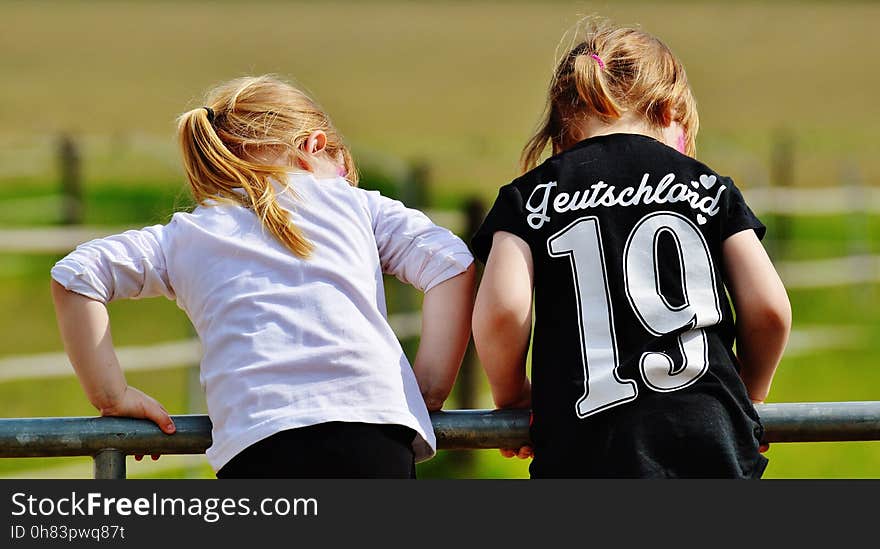 Girl in White Long Sleeve Shirt Beside Girl in Black T Shirt Holding Black Metal Handrail at Daytime