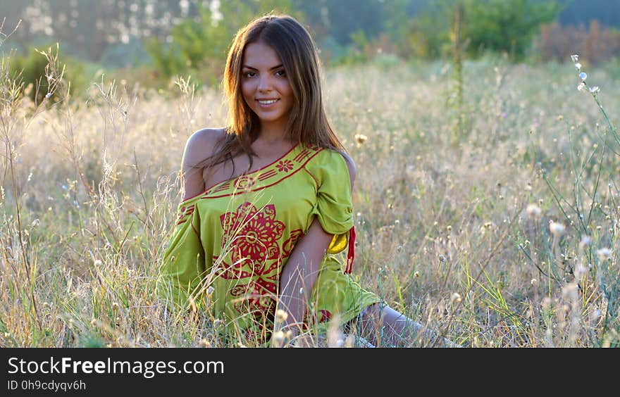 Woman Wearing Yellow and Red Dress Sitting on the Ground While Looking at the Camera