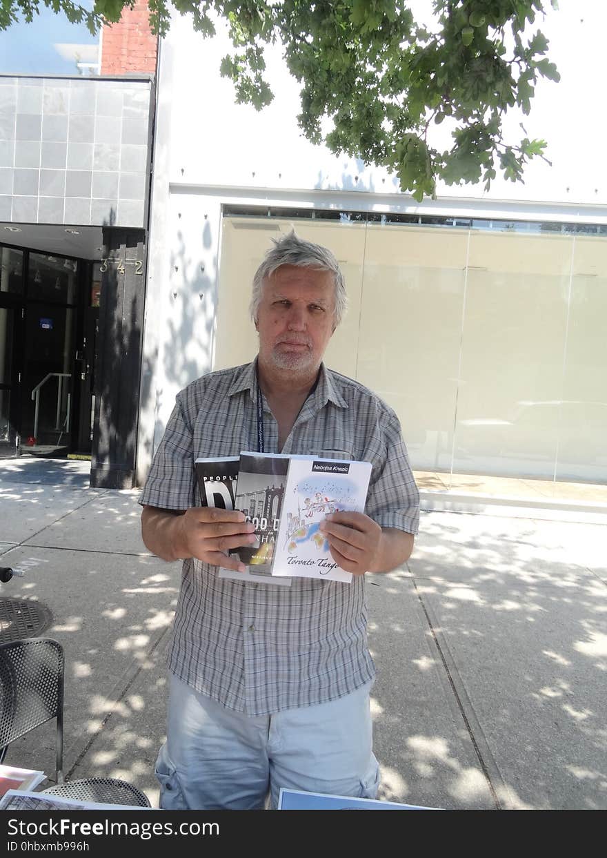 Journalist Nebojsa Knevic holds up three of the books he authored, 2017 08 09