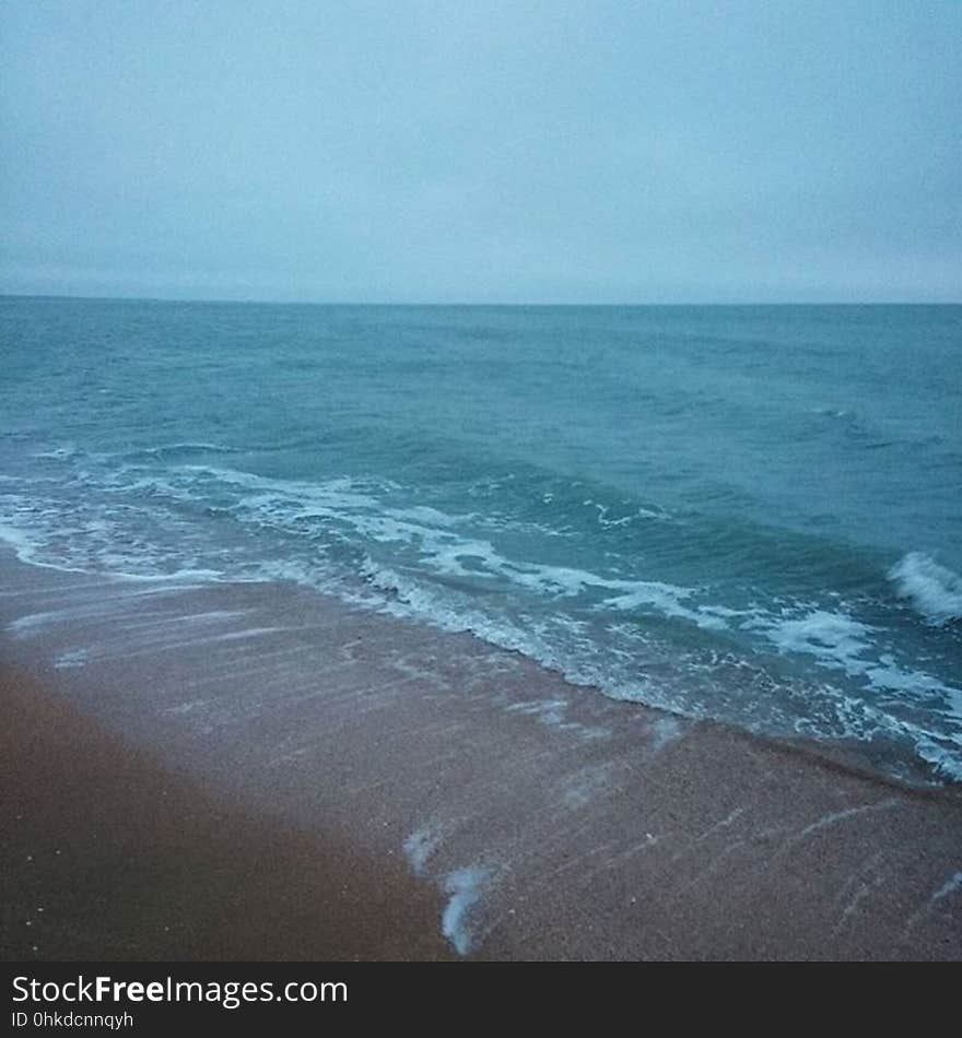 Waves coming ashore on a sandy beach at dusk.