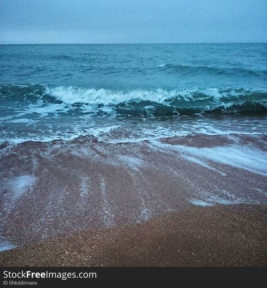 Incoming tide with waves breaking onto sandy beach with fine pebbles, blue cloudless sky. Incoming tide with waves breaking onto sandy beach with fine pebbles, blue cloudless sky.