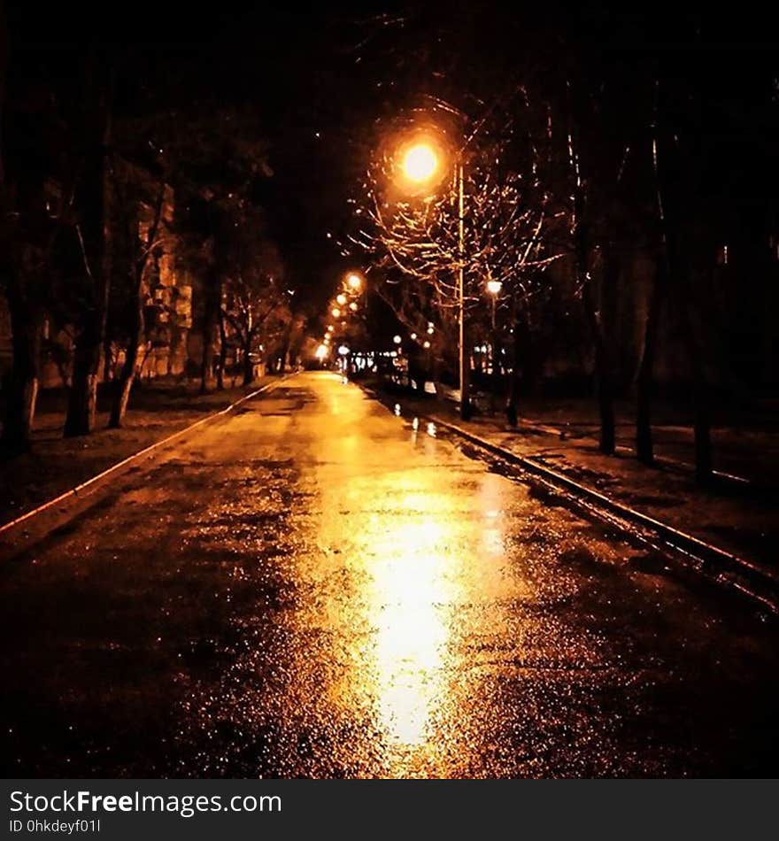 Long wet city street at night with shining orange light.