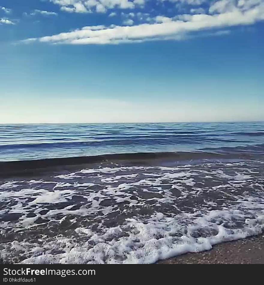 Scenic view of waves breaking on a beach with blue sky and cloudscape background.