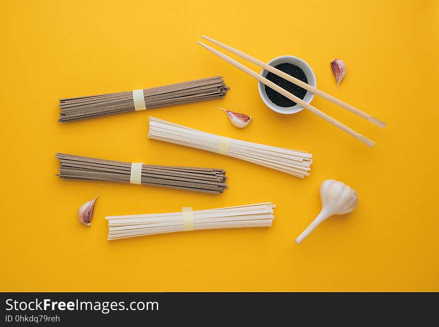 Asian noodles udon and soba, garlic, chopsticks, black sesame in a bowl on a bright yellow background. Minimalism. Flat lay.