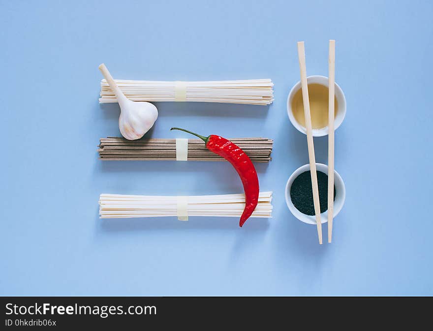 Asian noodles udon and soba, red chili, garlic, chopsticks, black sesame and rice vinegar in bowls on a bright blue background. Minimalism. Flat lay. Asian noodles udon and soba, red chili, garlic, chopsticks, black sesame and rice vinegar in bowls on a bright blue background. Minimalism. Flat lay.