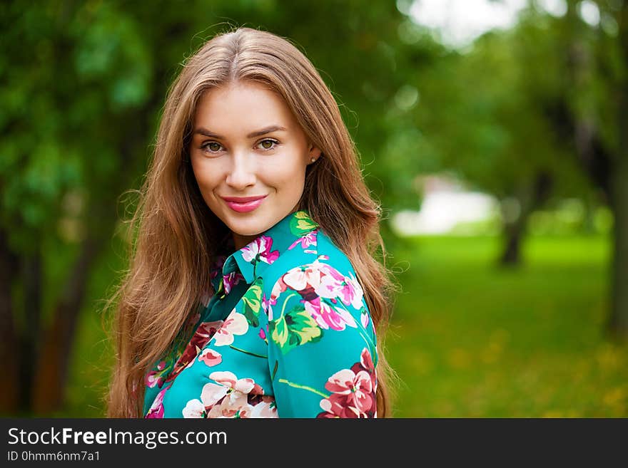 Young happy brunette woman in flowers blouse in the summer park. Young happy brunette woman in flowers blouse in the summer park