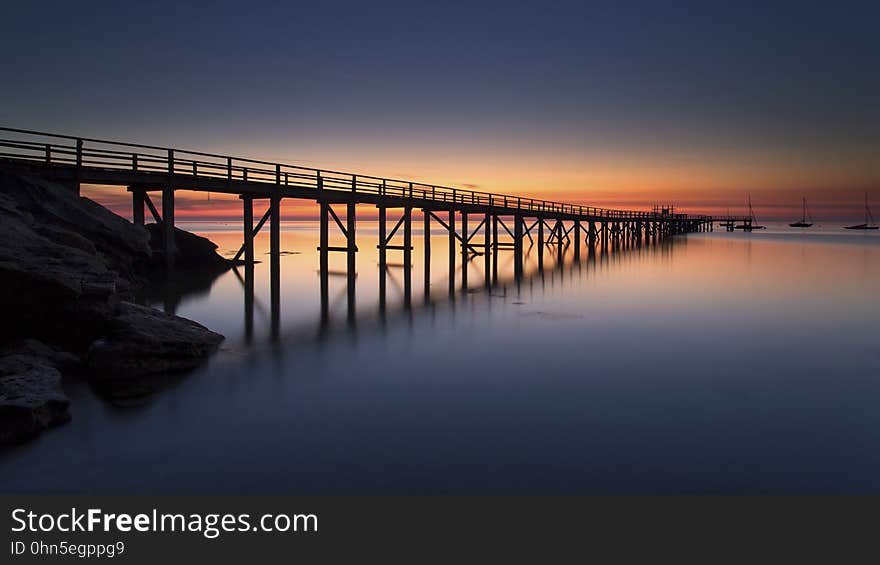 Sunset over wooden pier reflecting in calm waters.