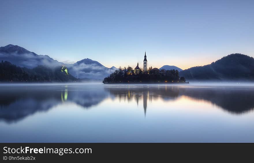 Mountains and a building are reflected in the still waters of a lake at dusk. Mountains and a building are reflected in the still waters of a lake at dusk.