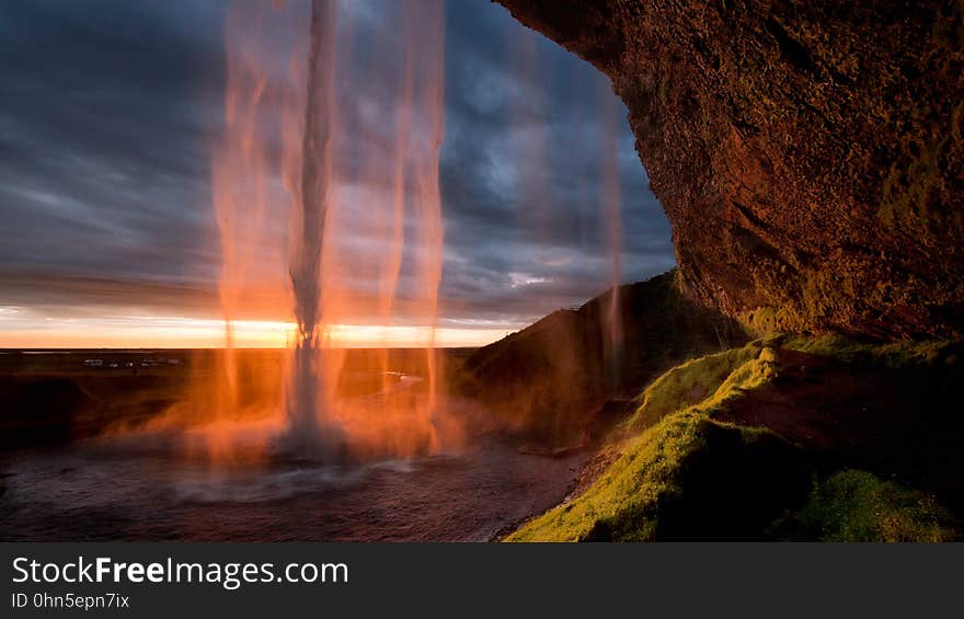 A waterfall by a rock and a sunset sky in the background. A waterfall by a rock and a sunset sky in the background.