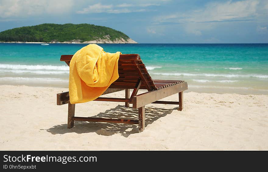 An empty wooden sunbed with a yellow towel on a sandy beach. An empty wooden sunbed with a yellow towel on a sandy beach.