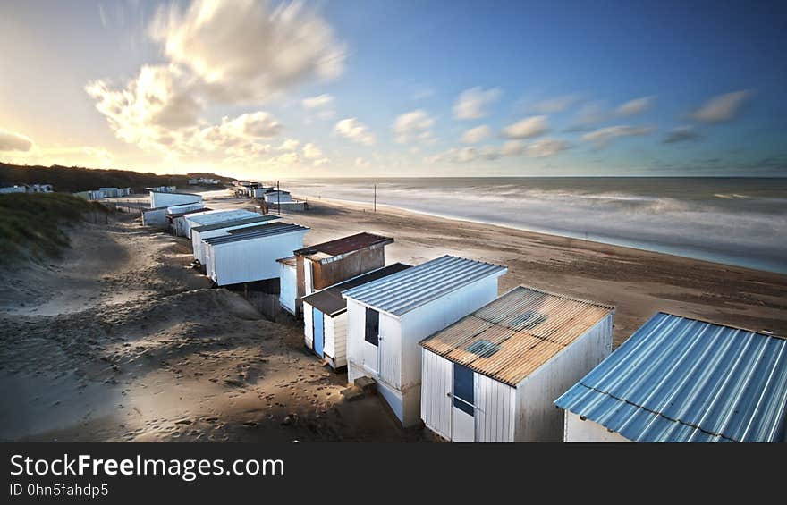 Row of changing huts built on sand dunes close to the beach and ocean, blue sky and fluffy clouds. Row of changing huts built on sand dunes close to the beach and ocean, blue sky and fluffy clouds.