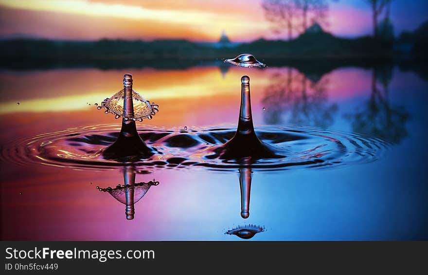 Two water splashes reflecting on colorful pool outdoors at sunset. Two water splashes reflecting on colorful pool outdoors at sunset.