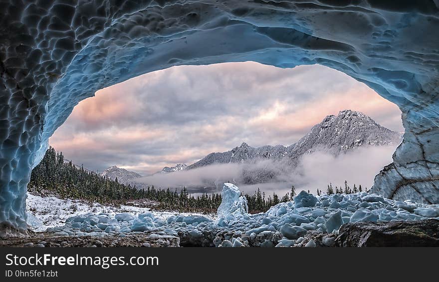 A frozen cave and a view of rocky mountain peaks in the background.