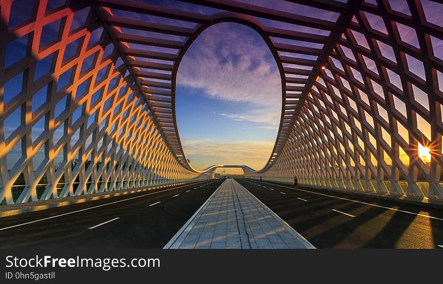 Two lanes receding over modern road bridge with unique architectural design at sunset. Two lanes receding over modern road bridge with unique architectural design at sunset.