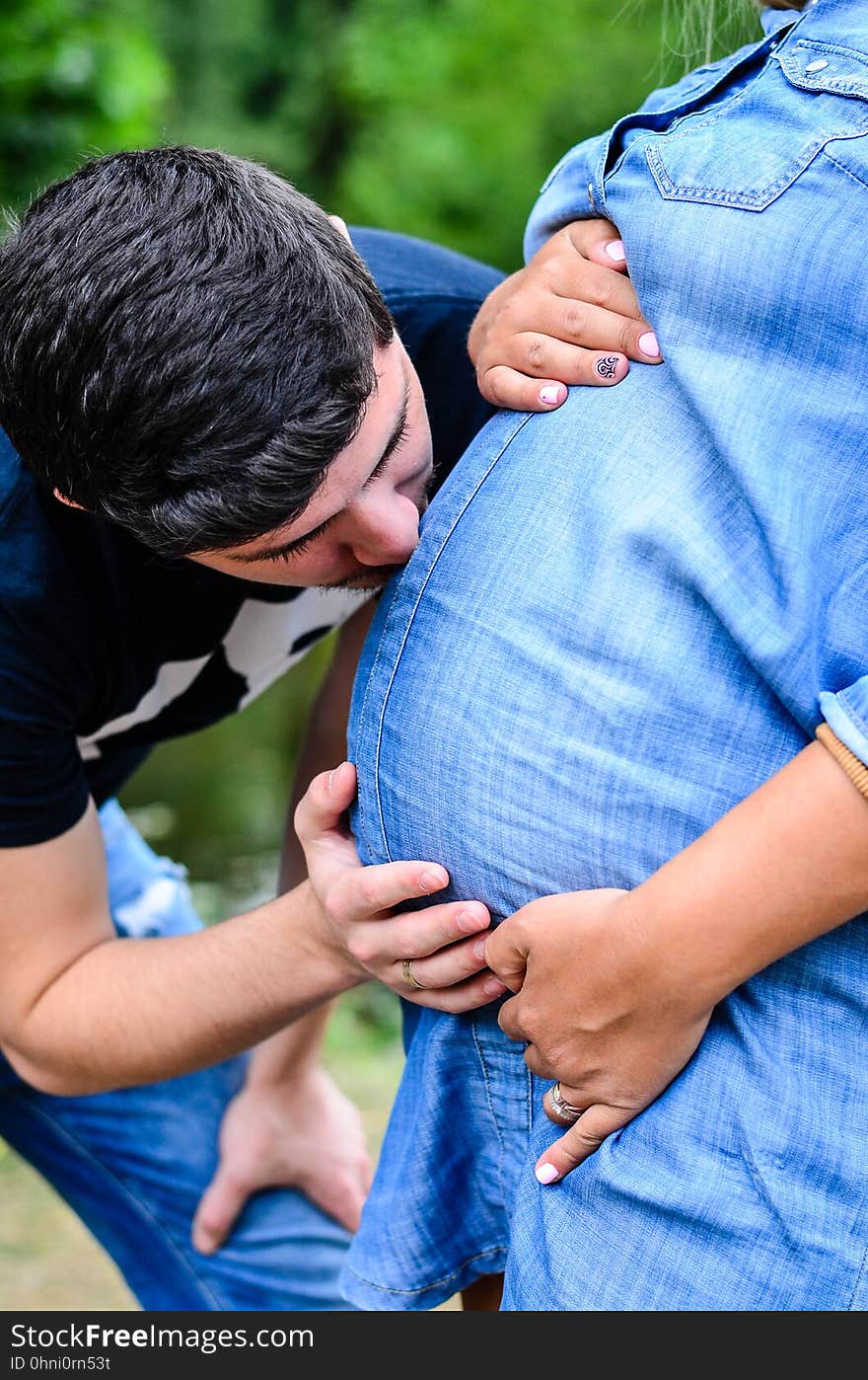 Happy and young pregnant couple hugging near a lake