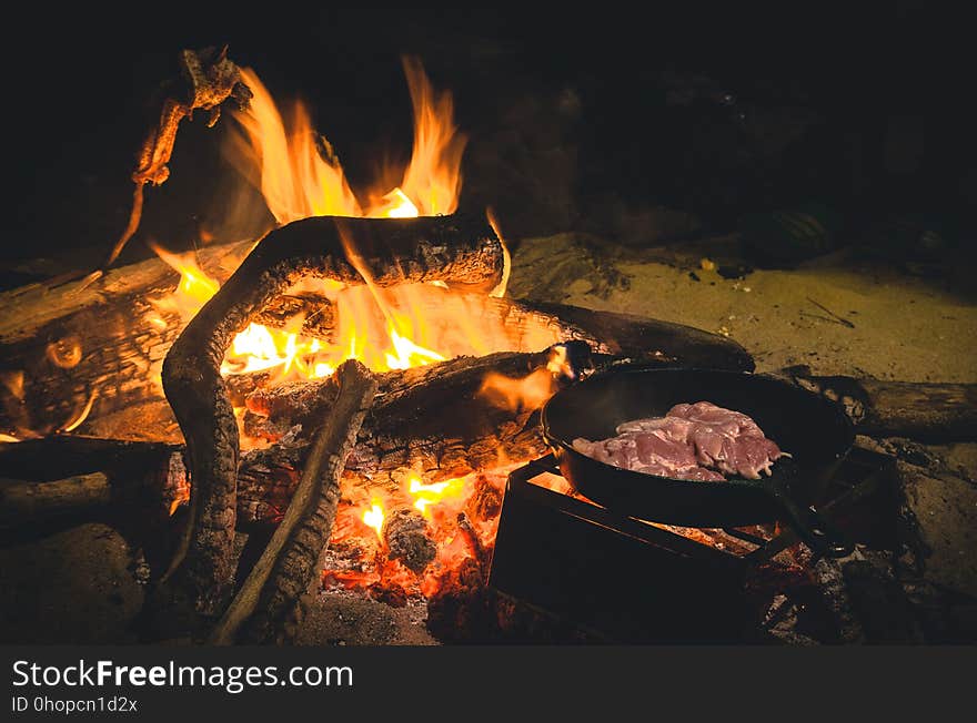 Close up of burning campfire with cast iron skillet full of meat at night. Close up of burning campfire with cast iron skillet full of meat at night.