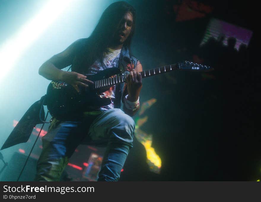 Male musician sitting playing electric guitar onstage during concert. Male musician sitting playing electric guitar onstage during concert.