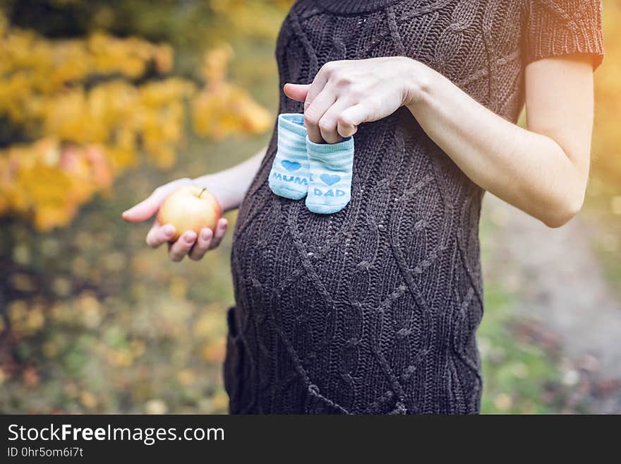 Portrait of pregnant woman with booties on her tummy in the autumn forest. Concept of pregnancy and the seasons