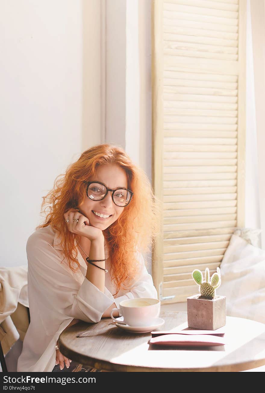 Red hair smiling young woman with cup of coffee in cafe. Morning. Copy space. Red hair smiling young woman with cup of coffee in cafe. Morning. Copy space